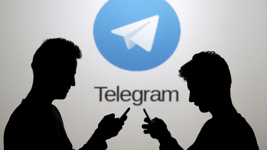 Two men pose with smartphones in front of a screen showing the Telegram logo in this picture illustration taken in Zenica